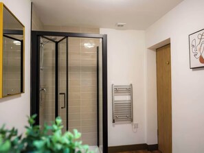 A bathroom with a glass shower enclosure, a towel rack, and a wooden door. - Aspen Apartment (Llanrwst)
