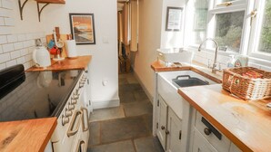 A kitchen with a stove, sink, and wooden countertops. There is a window with a view of trees and a door leading to another room. - Rock Cottage (Milnthorpe)