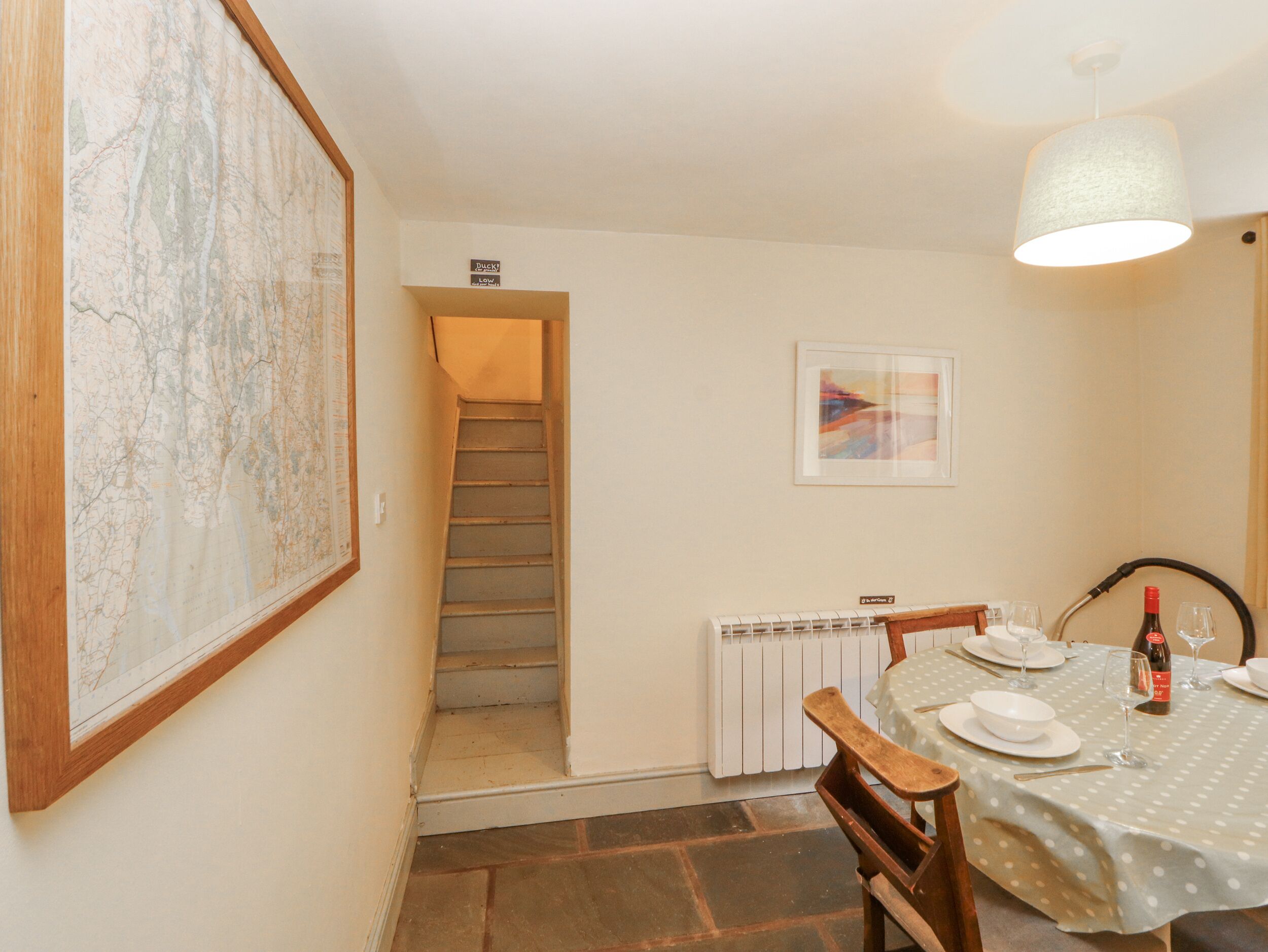 A dining area with a table set for two, a chair, a map on the wall, a staircase, and a radiator.
