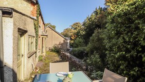 A table with a teapot, plates, and a mug in a garden setting with a stone wall and greenery. - Rock Cottage (Milnthorpe)