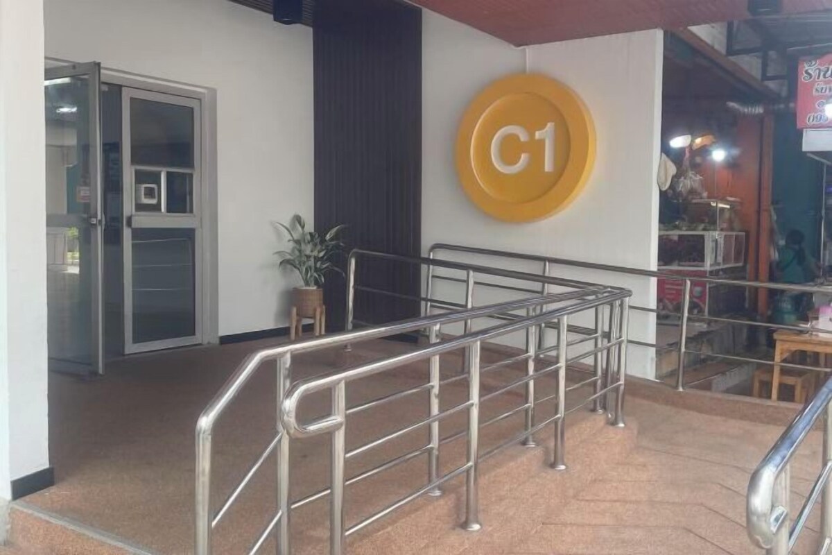 Een hotelentree met een metalen trap, een glazen deur en een geel rond bord met de letter 'C'.