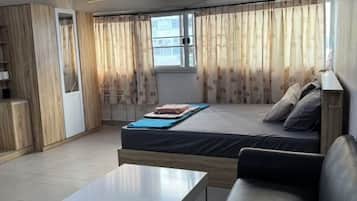 A room with a bed, a sofa, a table, and a window with curtains.