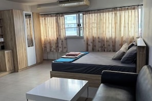 A room with a bed, a sofa, a table, and a window with curtains. - Impact Dailyroom C1,C9 by Anna (Pak Kret)