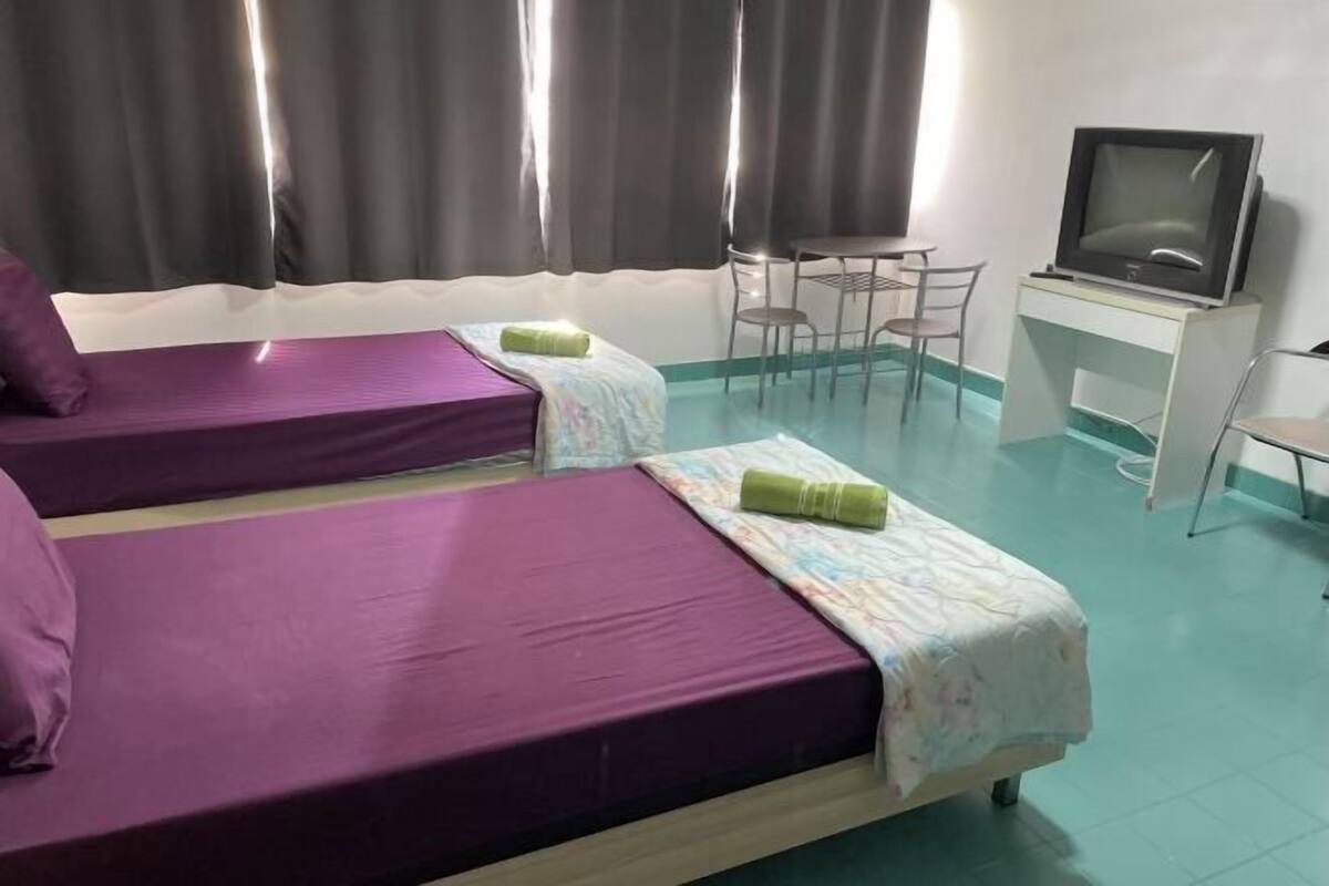 Una habitación con dos camas, un escritorio con televisor y una silla.