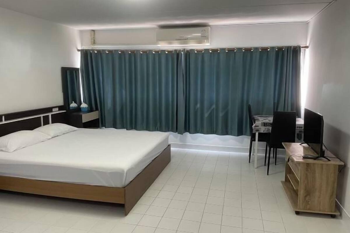 Habitación de hotel con cama, escritorio, silla, mueble pequeño y cortina.