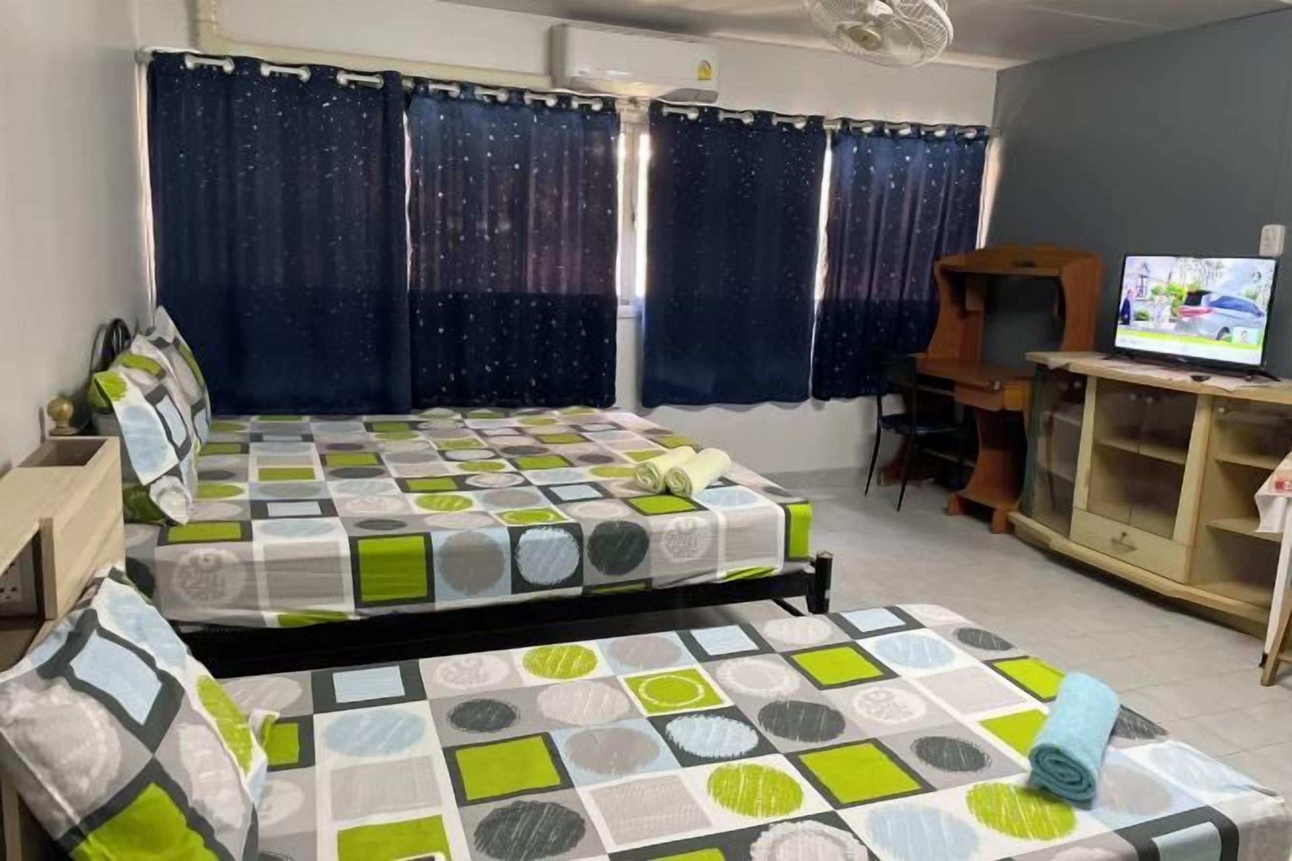 A bedroom with two beds, a television, and a desk.