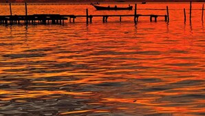 Un coucher de soleil sur une étendue d’eau calme, avec une jetée qui s’avance dans l’eau.