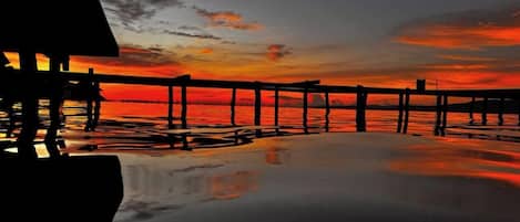 Une jetée s’avançant dans des eaux calmes au coucher du soleil, sous un ciel dégagé.