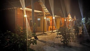 Un bâtiment en bois, doté d’un toit de chaume, entouré de plantes et bordé d’un chemin pavé.