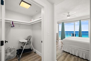 Ein Schlafzimmer mit Bett, Deckenventilator, Fenster mit Meerblick und Kleiderschrank mit Kinderwagen und Babykleidung.