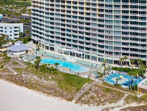 Ein großes Hotel mit mehreren Balkonen, einem zentralen Swimmingpool und einem Strandbereich.