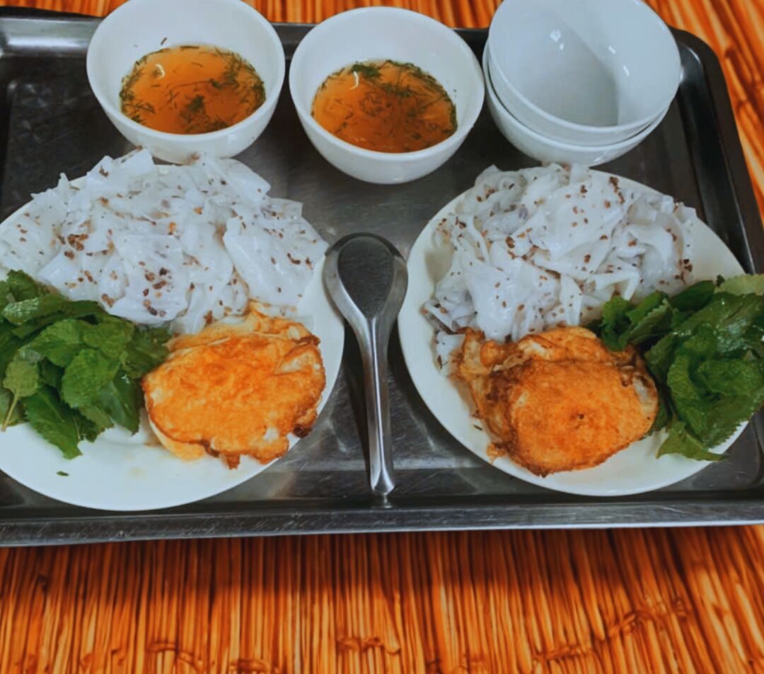 A tray with two plates of food, each with rice, fried items, and greens, and three small bowls of sauces.