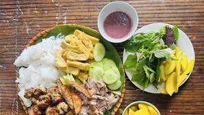 A meal with rice, fried items, grilled meat, cucumber slices, mango slices, and a bowl of sauce on a wooden table. - Suoi Rao Hao Huc Village (Ho Chi Minh City)