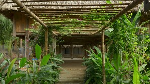 A covered walkway leading to a wooden structure with a thatched roof. - Suoi Rao Hao Huc Village (Ho Chi Minh City)