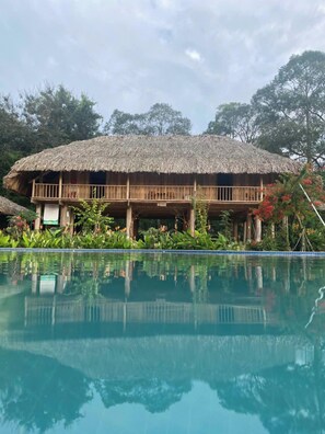 A thatched-roof building with a pool in front. - Suoi Rao Hao Huc Village (Ho Chi Minh City)
