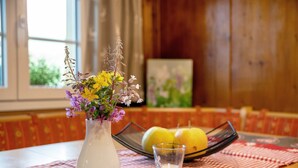 Ein Tisch mit einer weißen Vase voller Blumen, einem Glas Wasser und zwei Zitronen auf einer karierten Tischdecke.