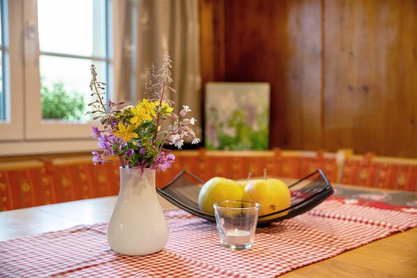 A table with a white vase of flowers, a glass of water, and two lemons on a checkered tablecloth. - Apartment 'Reesbauernhof - Fewo Abendrot' with Mountain View, Shared Terrace & Wi-Fi (Oberried)