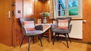 A wooden-paneled room with two grey upholstered chairs, a small table with a vase of flowers, and a window with a view of greenery. - Apartment 'Reesbauernhof - Fewo Abendrot' with Mountain View, Shared Terrace & Wi-Fi (Oberried)