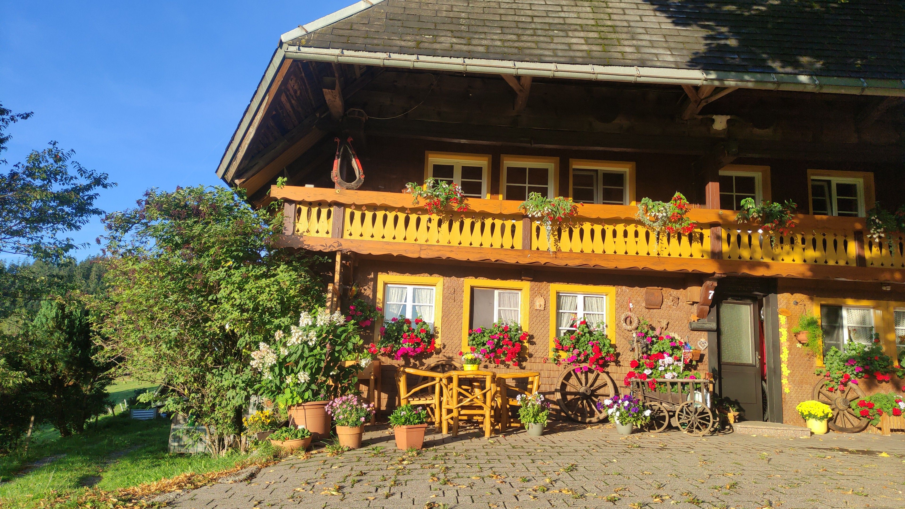 Un chalet traditionnel doté d’un balcon, de plantes en pot et d’une charrette en bois.