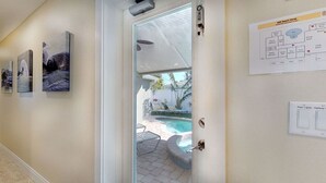Un pasillo con obras de arte enmarcadas, una puerta de vidrio que da a una zona de piscina y un plano de distribución de habitaciones en la pared.