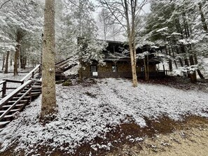 Eine Holzhütte in einem verschneiten Wald mit einer hölzernen Treppe, die zu einer Terrasse führt.