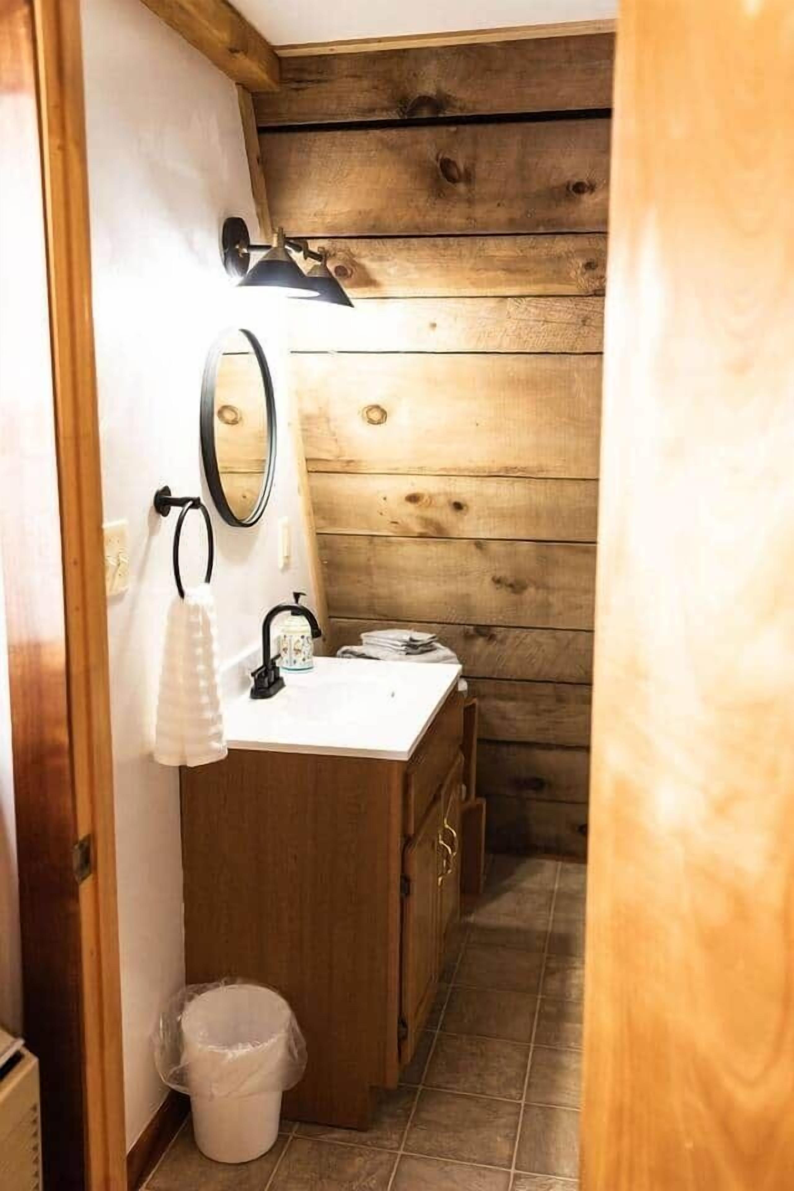 Un baño estrecho con paredes de madera, un lavamanos blanco, un espejo, una toalla y un cubo de basura.