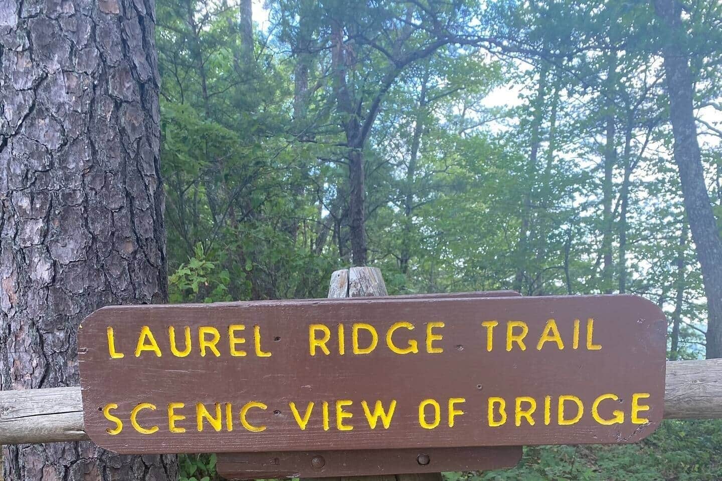Un panneau en bois avec une inscription jaune indiquant : « LAUREL RIDGE TRAIL – BELLE VUE SUR LE PONT ».