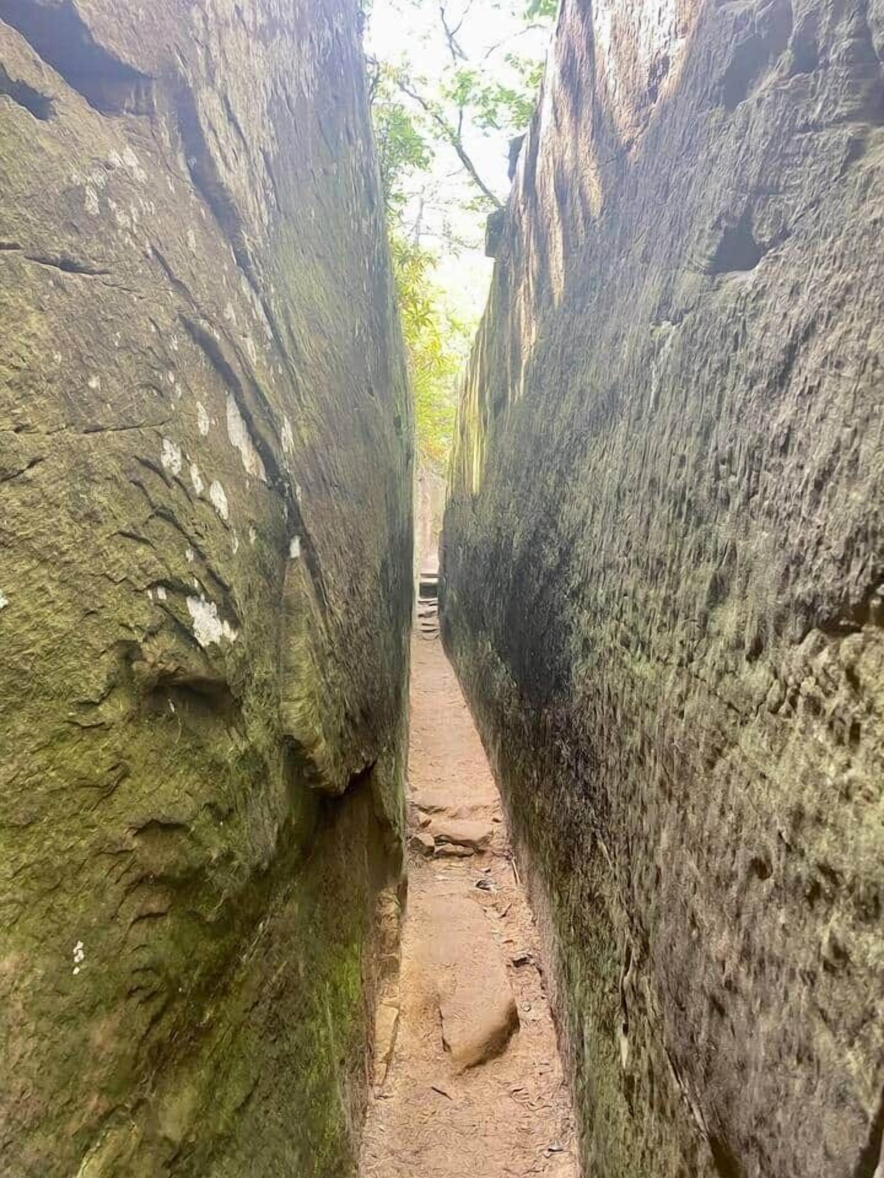 A narrow, rocky path between large boulders with moss growth.