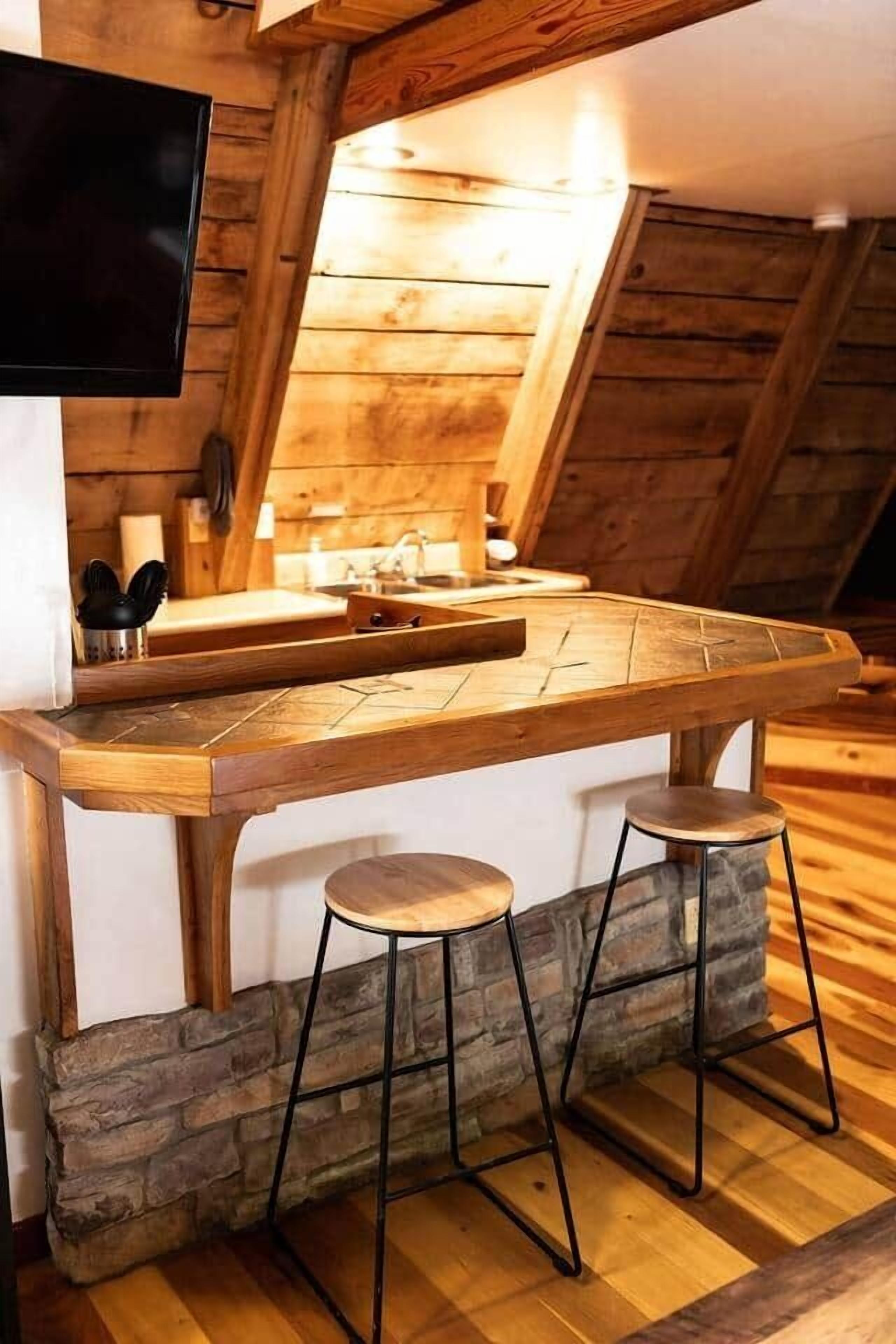 A wooden kitchen with a built-in TV, stone counter, and two stools.