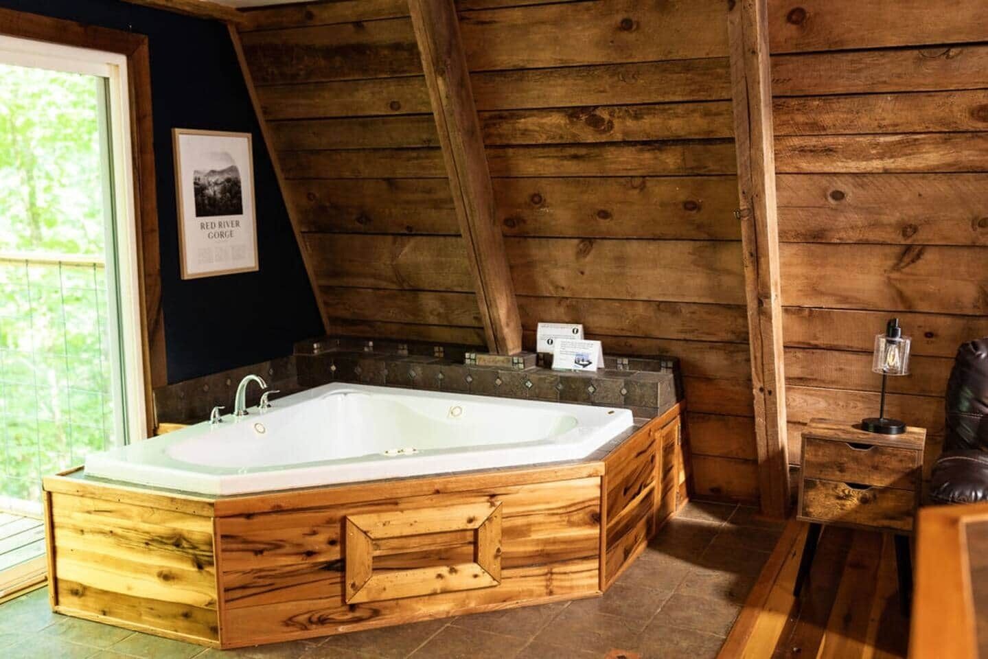 Une cabane en bois avec une grande baignoire en bois, une petite table avec une lampe et un tableau encadré au mur.