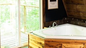 A wooden bathtub in a room with a large sliding glass door leading to a balcony. - Canoe Believe It Cabin | Indoor Jacuzzi Tub (Powell County)