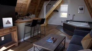 Avokeittiöllä varustettu, loft-tyylinen olohuone, jossa on ruokapöytä tuoleineen, sohva, sohvapöytä ja portaat, jotka johtavat ylemmälle tasolle.