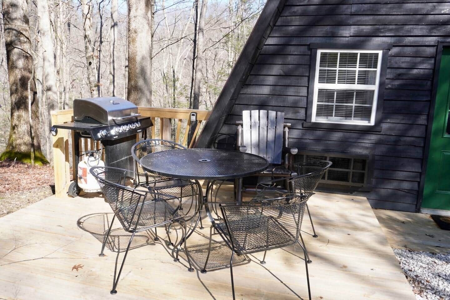 An outdoor patio with a round metal table and chairs, a grill, and a green door.