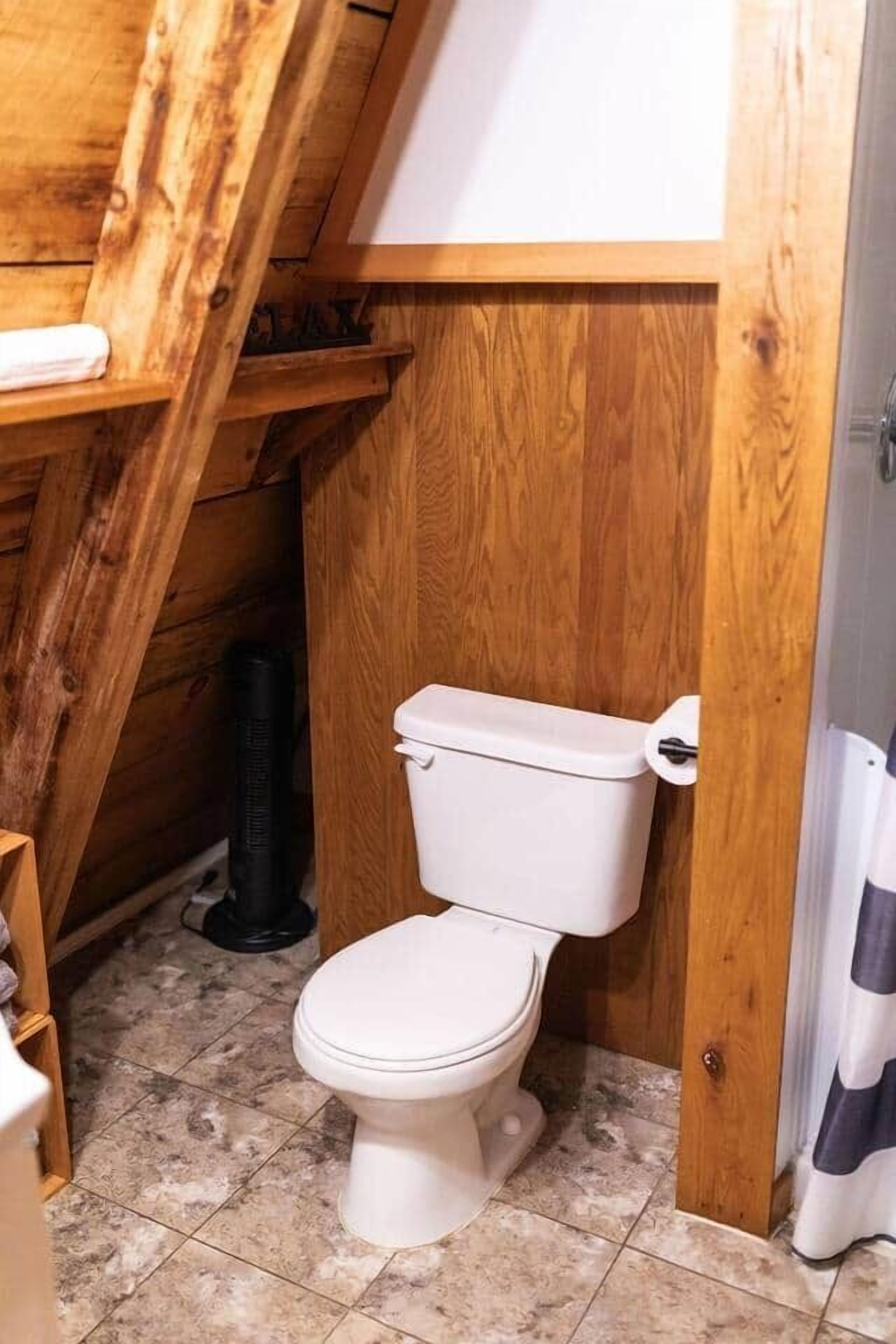 A small, rustic bathroom with a wooden ceiling and a white toilet.