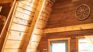 A cozy attic room with a wooden sloped ceiling, a leather sofa, a wooden dining table, and a window with curtains.