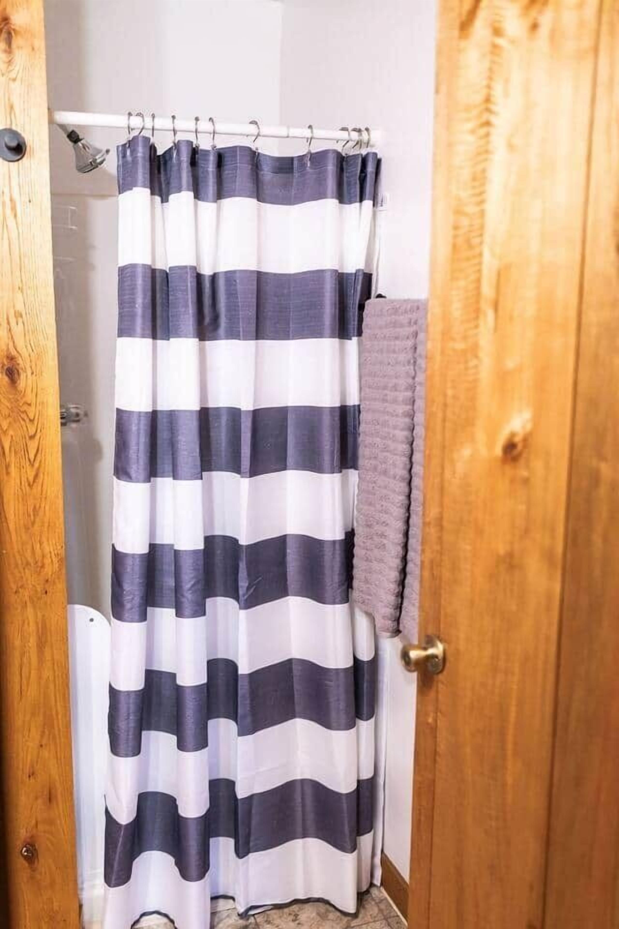 A bathroom with a striped shower curtain, a wooden door, and a towel rack.