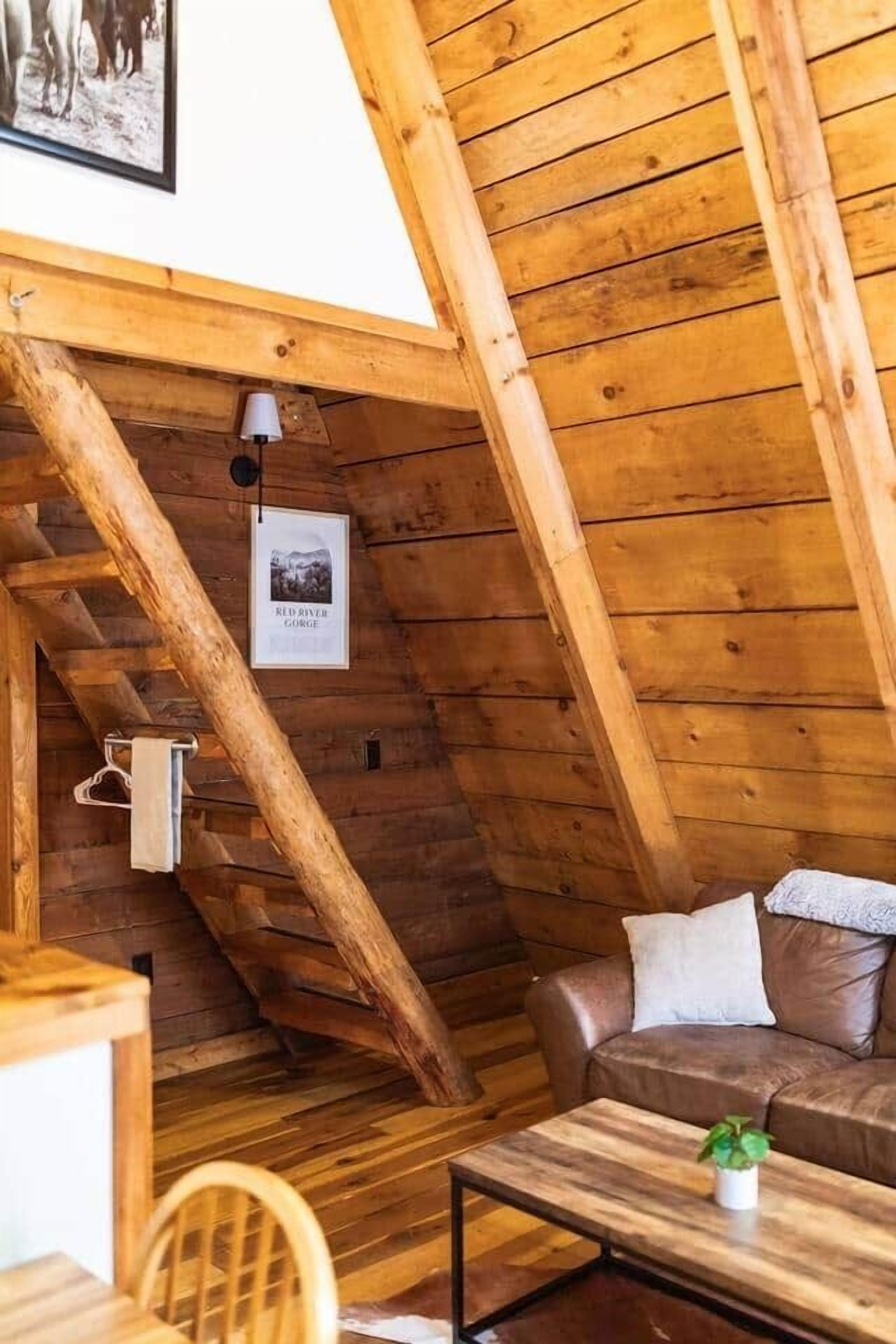 Une chambre à coucher confortable, aménagée dans un espace mansardé avec un plafond en pente, des poutres en bois, un canapé en cuir marron, une petite table avec une plante et un tableau encadré accroché au mur.