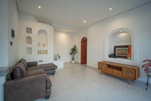 A modern living room with a brown leather sofa, a wooden console table, and a large painting on the wall. - 3 bed room Villa Rice View Terrace in Bali (Sukawati)