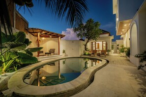 Ein Schwimmbecken mit geschwungener Form, umgeben von einer Terrasse mit Sitzgelegenheiten und Pflanzen.