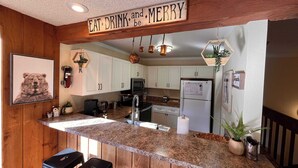 Eine Küche mit einer Holztresen-Bar, Wandbild mit Bärenmotiv und einem Schild mit der Aufschrift 'Eat, Drink, and be Merry'.