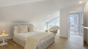 Une chambre avec un grand lit, une table de chevet avec une lampe, une chaise et une vue sur l’extérieur.