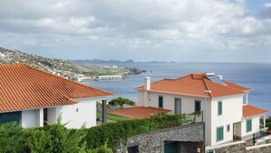 Une villa côtière avec un toit recouvert de tuiles rouges, des murs blancs et une vue sur la mer et les montagnes lointaines.
