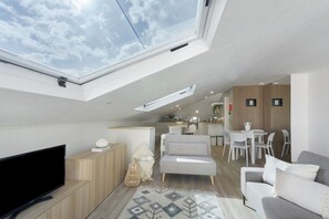 Ein moderner Wohnraum mit Oberlicht, Flachbildfernseher, Sofa, Essbereich und Küche.
