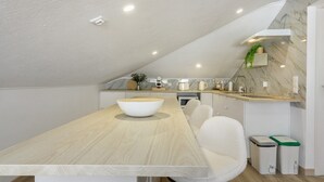 Une cuisine moderne avec un plan de travail en bois, des chaises blanches et un saladier blanc.