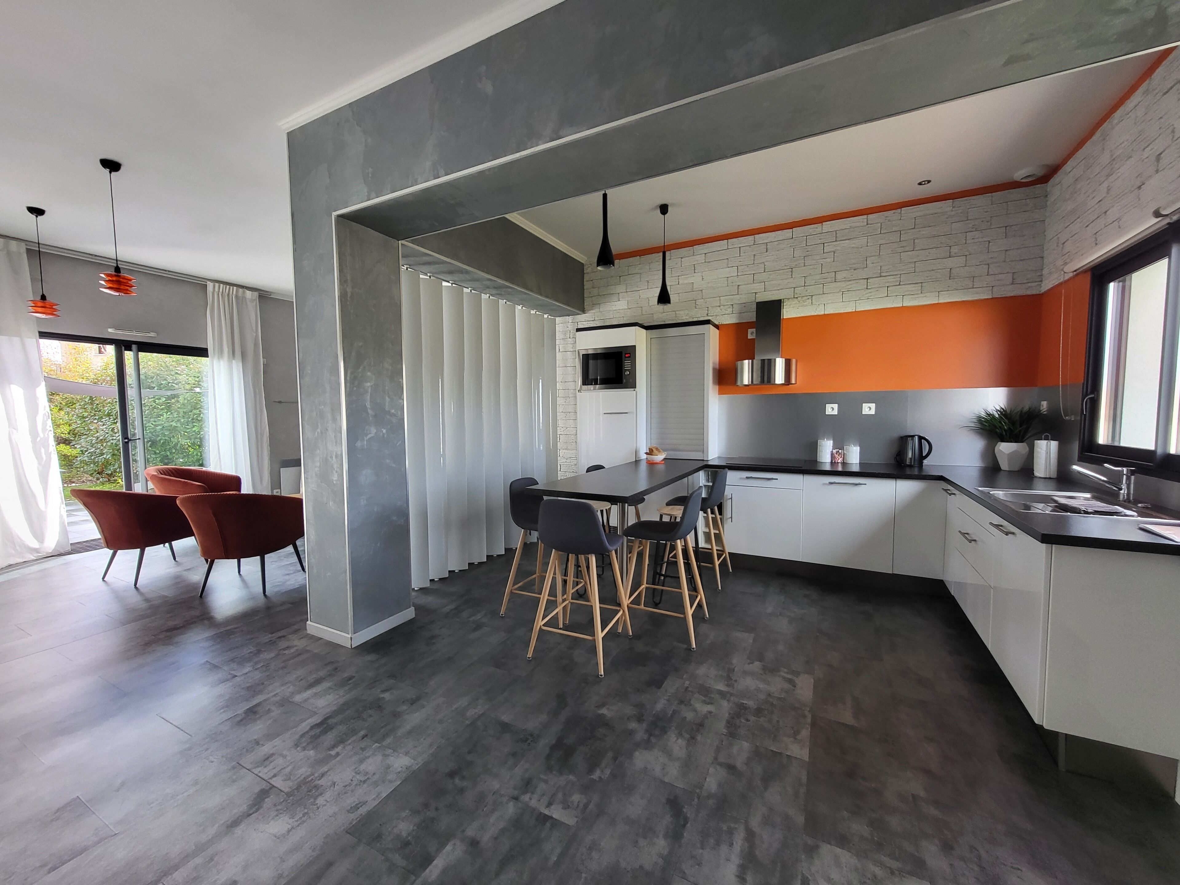 Una cocina moderna con una isla central, taburetes de bar y un comedor con sillas rojas.