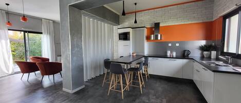 Una cocina moderna con una isla central, taburetes de bar y un comedor con sillas rojas.