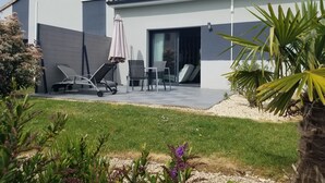 Een modern huis met een terras, zitplaatsen buiten en een tuin.