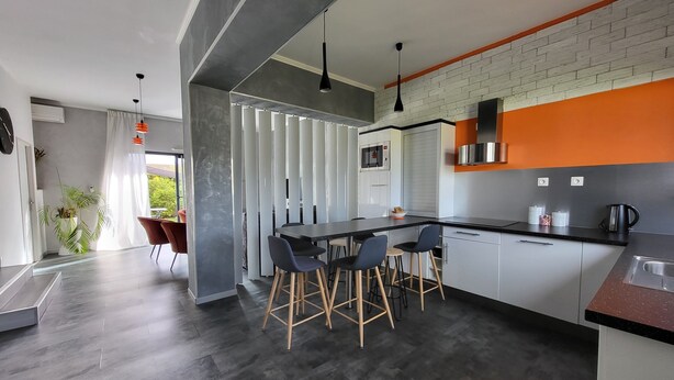 Een moderne keuken met een zwart aanrecht, witte kasten en een accentmuur van baksteen.