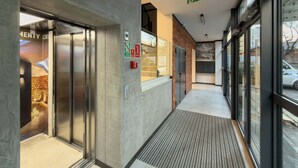 An interior corridor with an elevator, a fire alarm, and a glass door leading to a room. - Modern Apartment | Air Conditioning | Spa and Gym | Parking. (Wrocław)