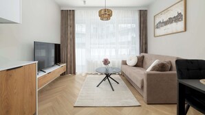 A modern living room with a flat-screen TV, a sofa, a coffee table, and a large window with sheer curtains. - Modern Apartment | Air Conditioning | Spa and Gym | Parking. (Wrocław)